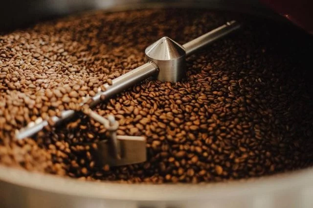 Kaffe trummel fylld med nyrostat kaffe som rör sig runt med hjälp av en centralt fäst mekanisk arm som rör om kaffet som svalnar.